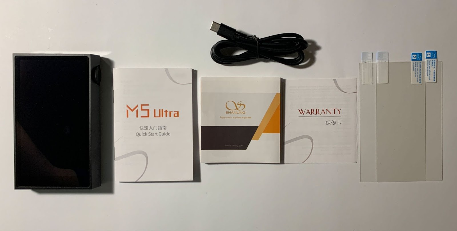 Opening the box, we see the player itself from above, lying in a molded foam tray; there is a black rope on the side for easy removal.Below is the entire package: in the middle is a flat box with documentation and protective films, and even lower is a rectangular box with a cable. 